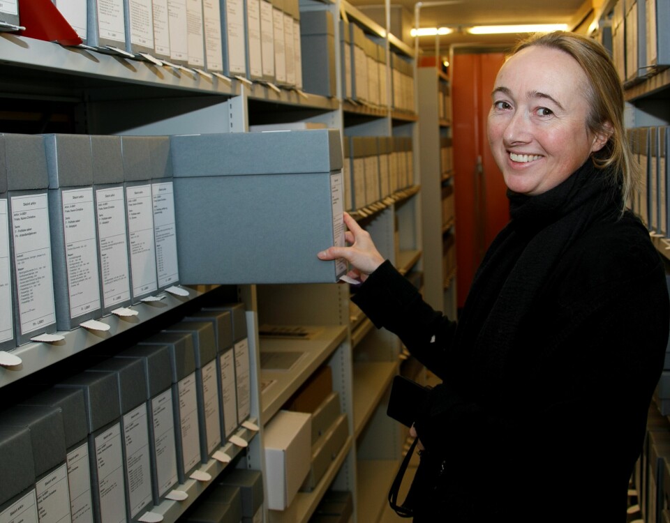 Heidi Rohde Rafto holder en arkivboks opp mot en arkivhylle
