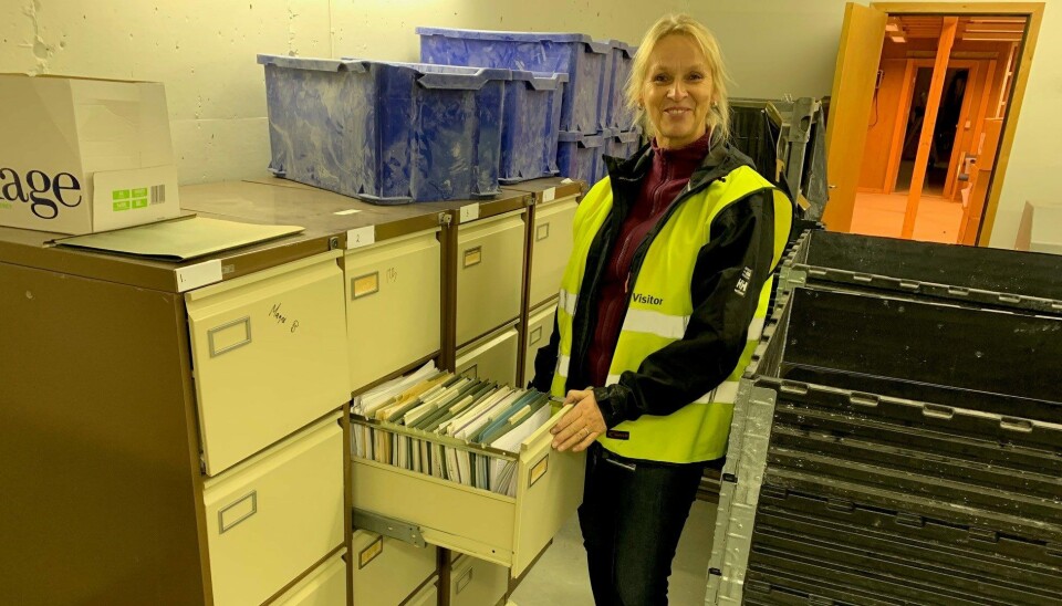 Kvinne står foran et arkivskap. Hun har på seg yttertøy og refleksvest og ser mot kameraet.