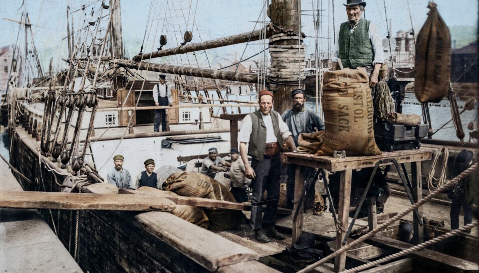 Bilde som viser en seilskute og menn som arbeider med å laste sekker av og på.