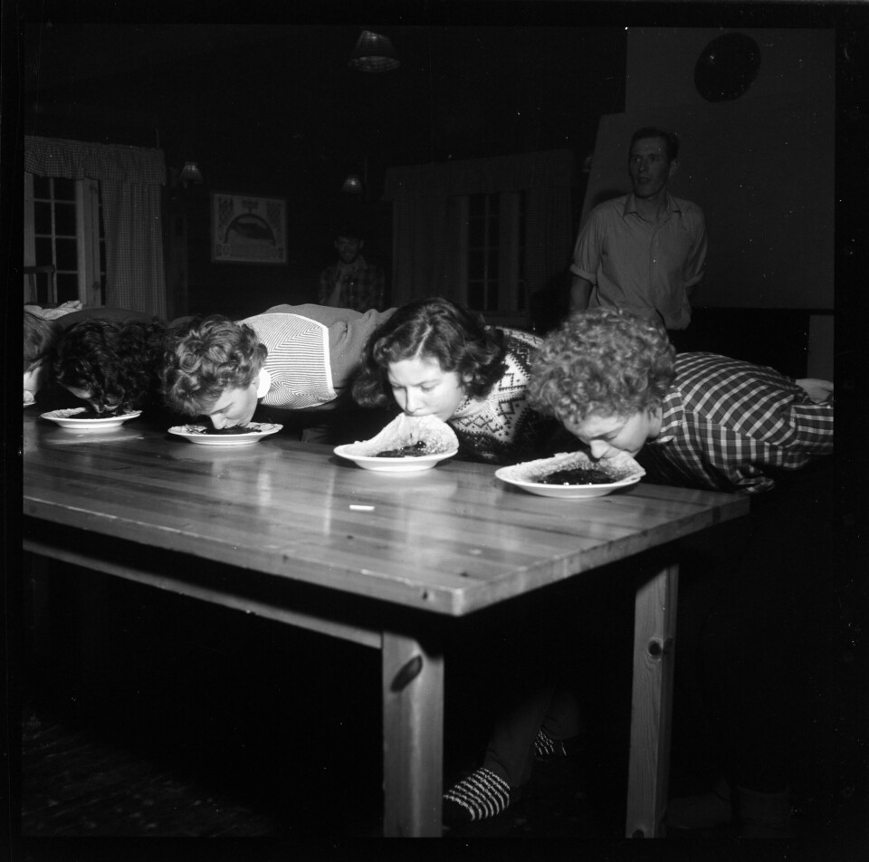 STUDENTHYTTA 1957: Tullete aktiviteter var en del av det å være student også på femtitallet. Her kan det se ut til at det var en egen kvinneklasse i spise-uten-hjelp-av-hendene-konkurransen på Studenthytta. Sort-hvit-bildet viser fire jenter som forsøker å spise hver sin pannekake uten å bruke hender.