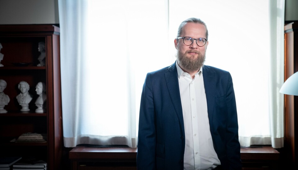 Vi har et mål om å være nasjonalbibliotek for fem millioner innbyggere, og de nås på forskjellige måter, sier nasjonalbibliotekar Aslak Sira Myhre. En mann kledd i dressjakke og hvit skjorte uten slips står oppstilt foran et vindu med gjennomsiktig gardin. Han ser mot kameraet. Han har skjegg, briller og lang hår som er dratt bakover i en hestehale.