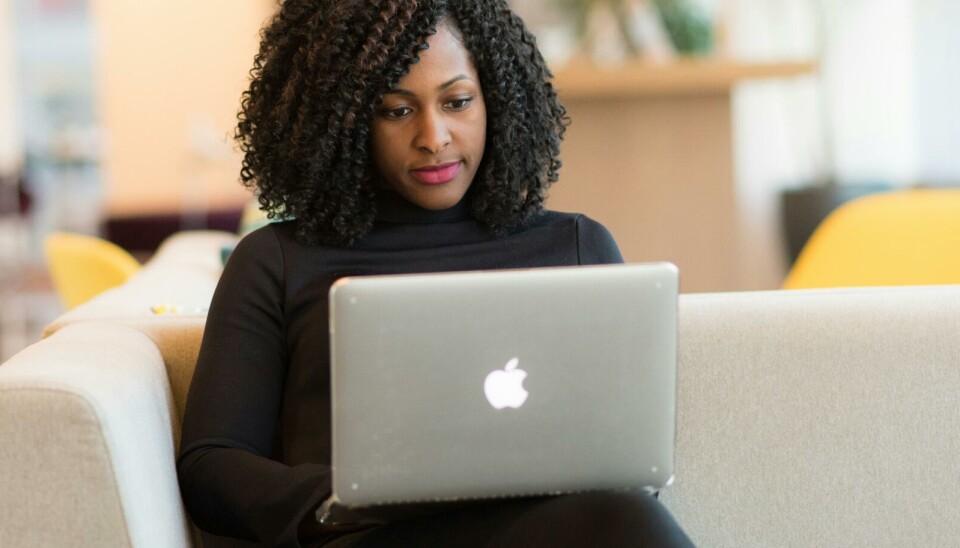 Webinar om bevaring og kassasjon Bildet viser en kvinne med mørkt krøllete hår og sorte klær som sitter i en sofa med en bærbar pc i fanget. Hun ser konsentrert ut.