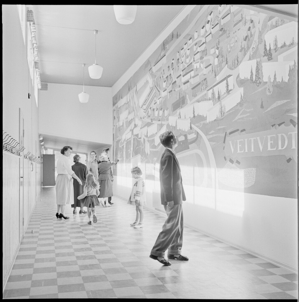 FOR FREMTIDEN: Bildet er fra åpningen av Veitvedt skole i 1958, tatt for NÅ nr. 35 1958. Bildet er hentet fra Digitalarkivet. Sort-hvit-bildet viser noen mennesker som er i en flott dekorert gang. Det er rutete gulvbelegg, høyt under taket og et stort veggmaleri på den ene veggen.