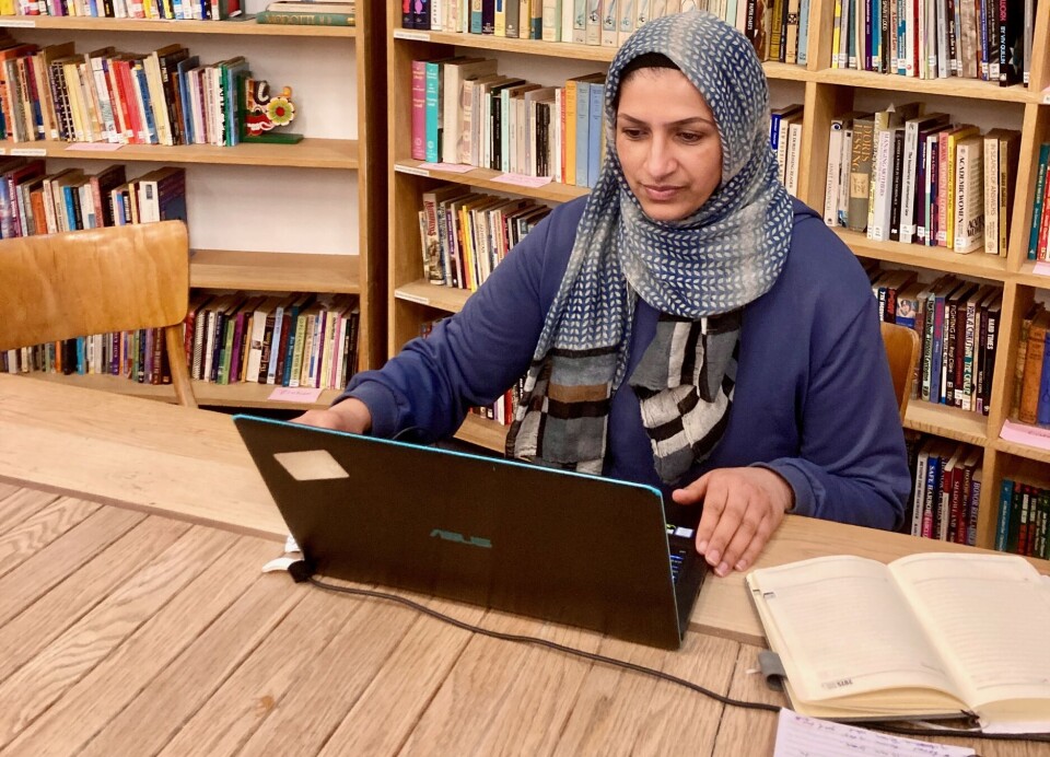 Syma Ahmed har vært ansatt siden 2007 og driver prosjekter for BME (black & minority ethnic) kvinner. En kvinne ved et bord med en laptop og noen bøker. Hun har på seg blå jakke og en hijab