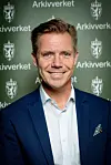 Portrett av avdelingsdirektør Stian Norli foran en grønn vegg med Arkivverket-logoer.