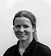 Smilende kvinne i svart-hvitt foran en lys vegg