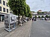 Utendørsutstilling med fotoplakater langs en gate i Arendal sentrum, med folk som går forbi.