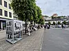 Utendørsutstilling med fotoplakater langs en gate i Arendal sentrum, med folk som går forbi.