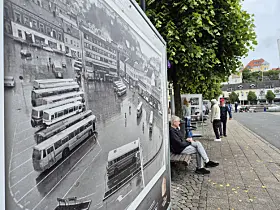 Stort svart-hvitt bilde på fortauet med folk som går forbi i en bygateg.