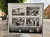 Informasjonstavle med fire historiske svart-hvite bilder og tekst ved en gate.