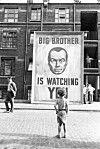 Stort plakat med «Big Brother is Watching You» på en bygning, med barn og voksne foran i en gate.