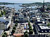 Utsikt over bysentrum med havn, kirketårn, båter og fjord i bakgrunnen.