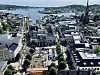 Utsikt over bysentrum med havn, kirketårn, båter og fjord i bakgrunnen.