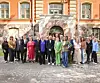 En gruppe voksne står samlet foran en historisk bygning med brosteinsbelagt plass.
