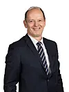 Smilende mann i mørk dress og stripet slips mot hvit bakgrunn.