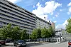 Moderne kontorbygg langs en bygate med trær, biler og blå himmel.